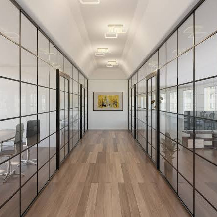 A modern office hallway with glass-walled cubicles, light wood flooring, and a small framed artwork on the back wall.